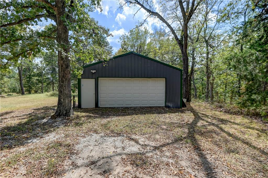 Dark detached garage with a wide white overhead door, framed by mature trees.