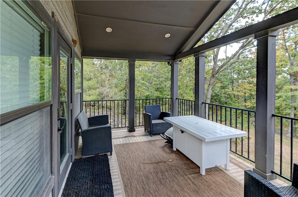 Covered deck with wicker seating and a white table overlooking trees.