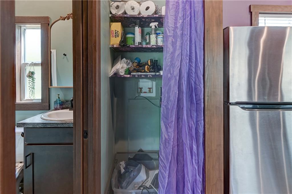 Laundry area with open supply shelves and a purple curtain beside a stainless-steel refrigerator.