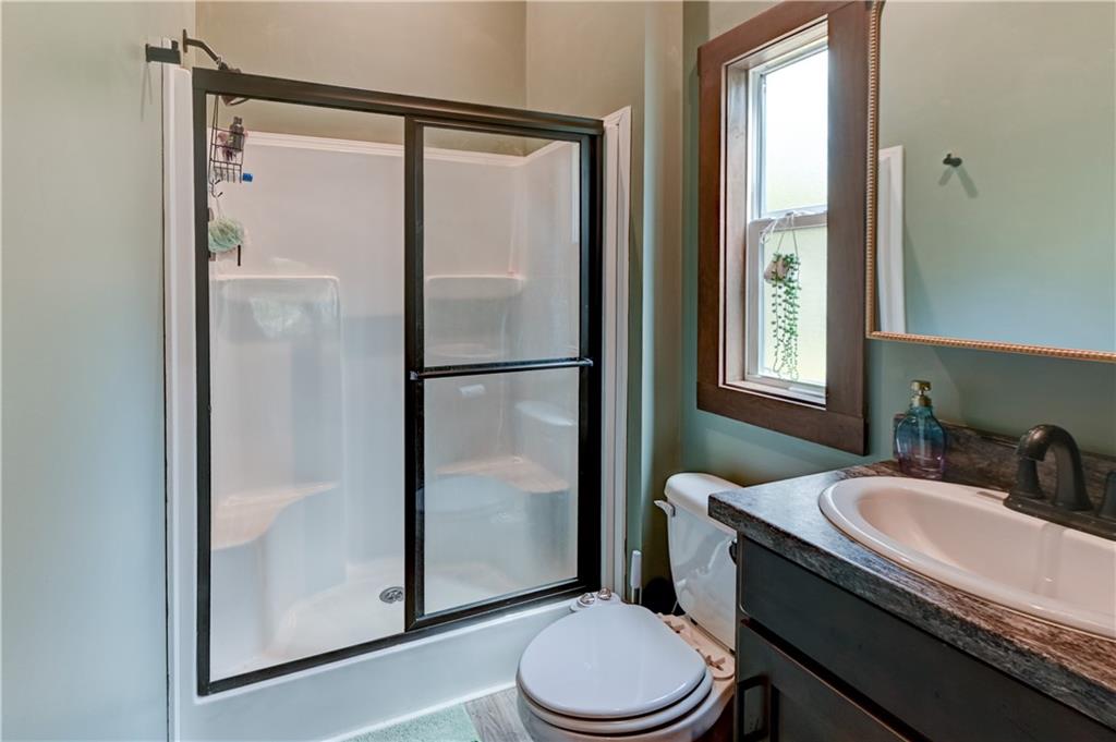 Bathroom with black-framed glass shower doors, dark vanity, and wood-trimmed window.
