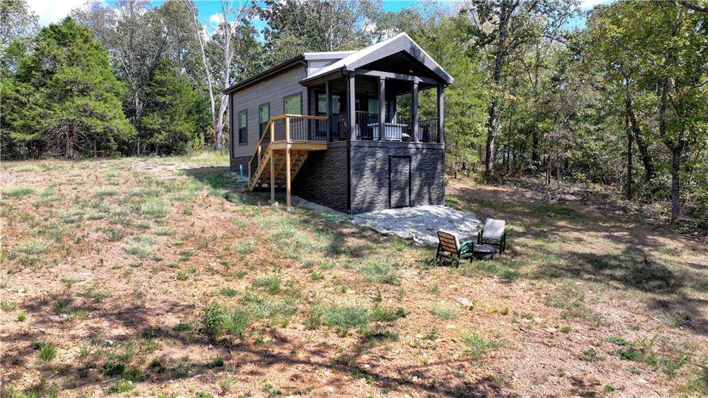 Modern cabin with a raised covered porch and wooden stairs on a wooded lot.
