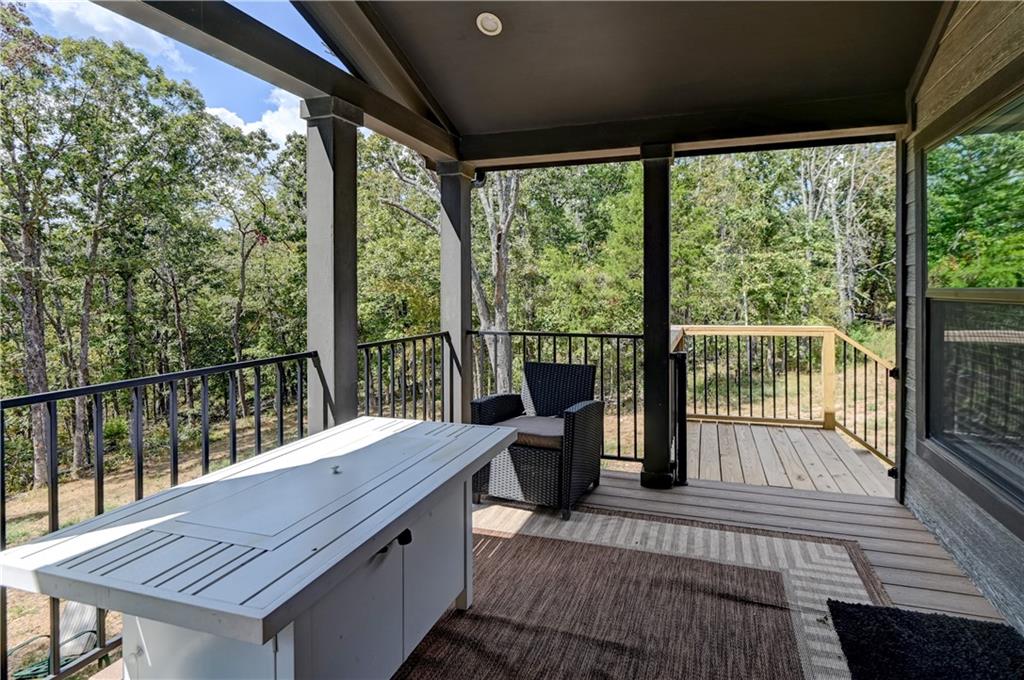 Covered deck with a white table and woven chair overlooking trees.
