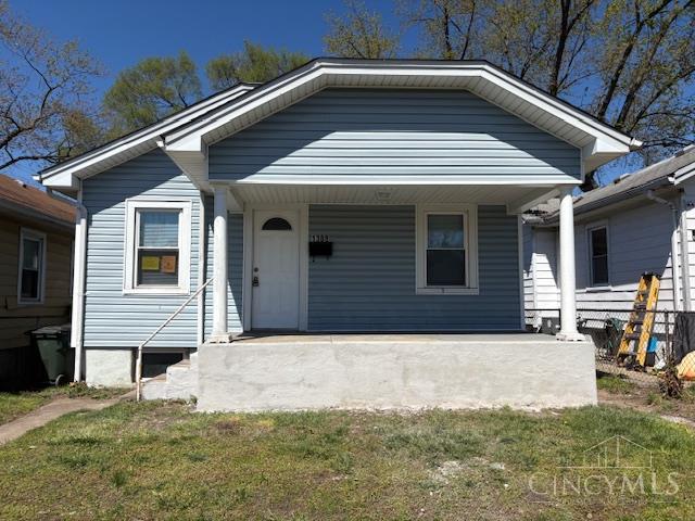Blue-gray single-story house with white trim, a covered porch, and a grassy front yard.