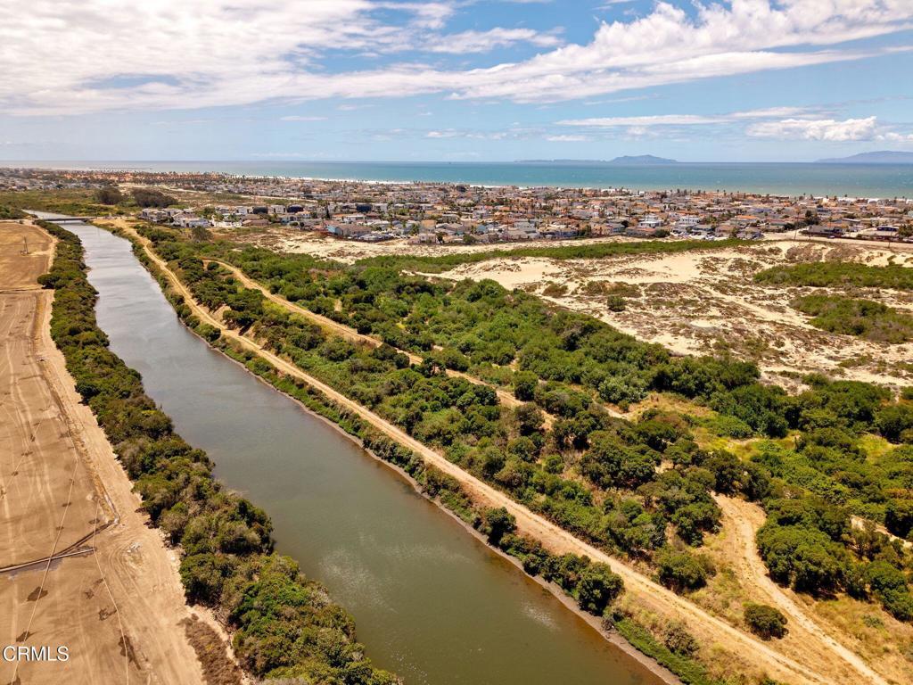 Aerial view of a canal leading toward Oxnard’s coastline, with neighborhoods and sandy dunes.
