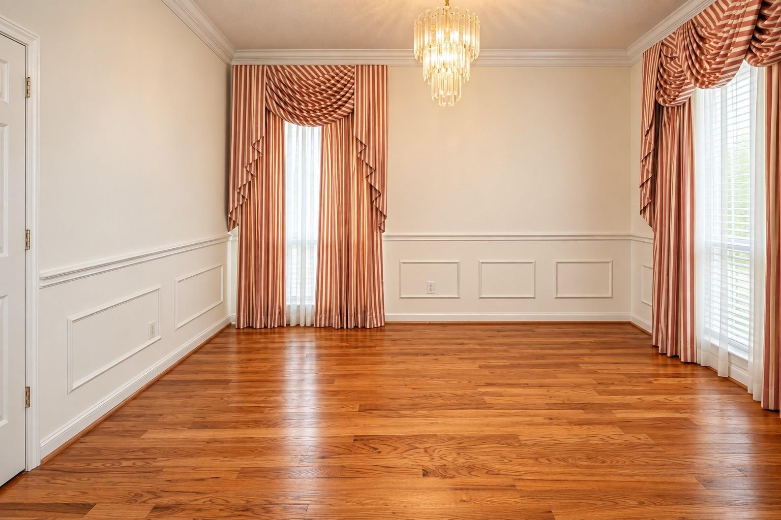 Empty formal room with hardwood floors, striped drapes, and a crystal chandelier.