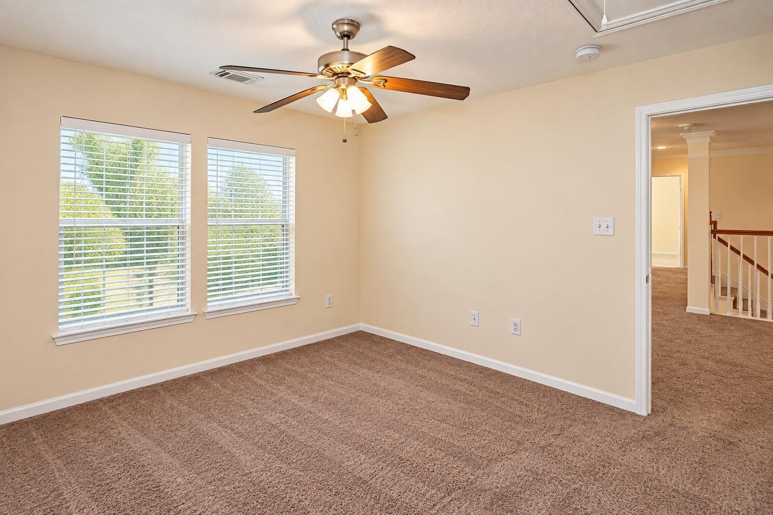 Empty carpeted room with two curtained windows, a ceiling fan, and a doorway to the landing.