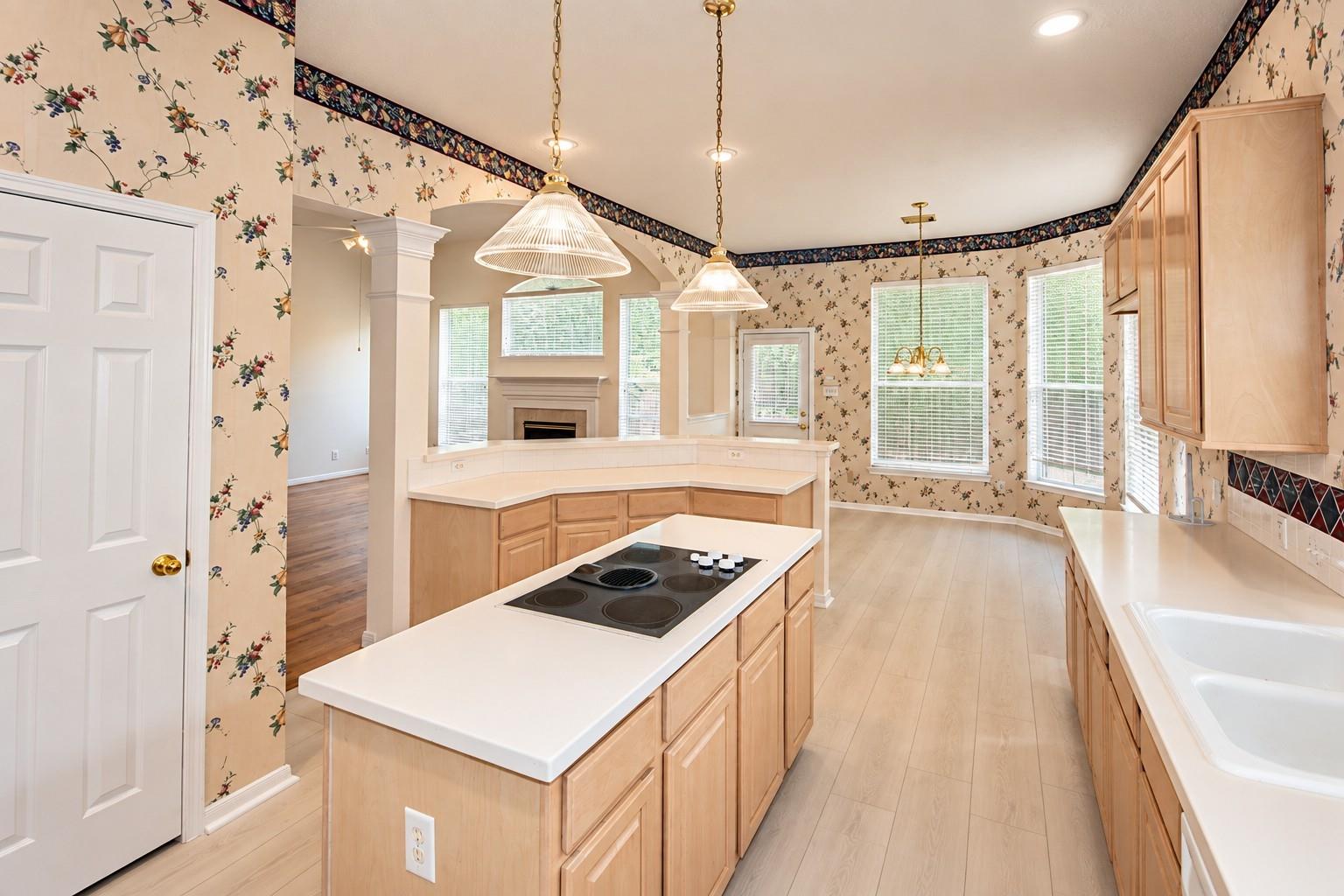 Kitchen with a central cooktop island, light wood cabinets, and floral wallpaper.