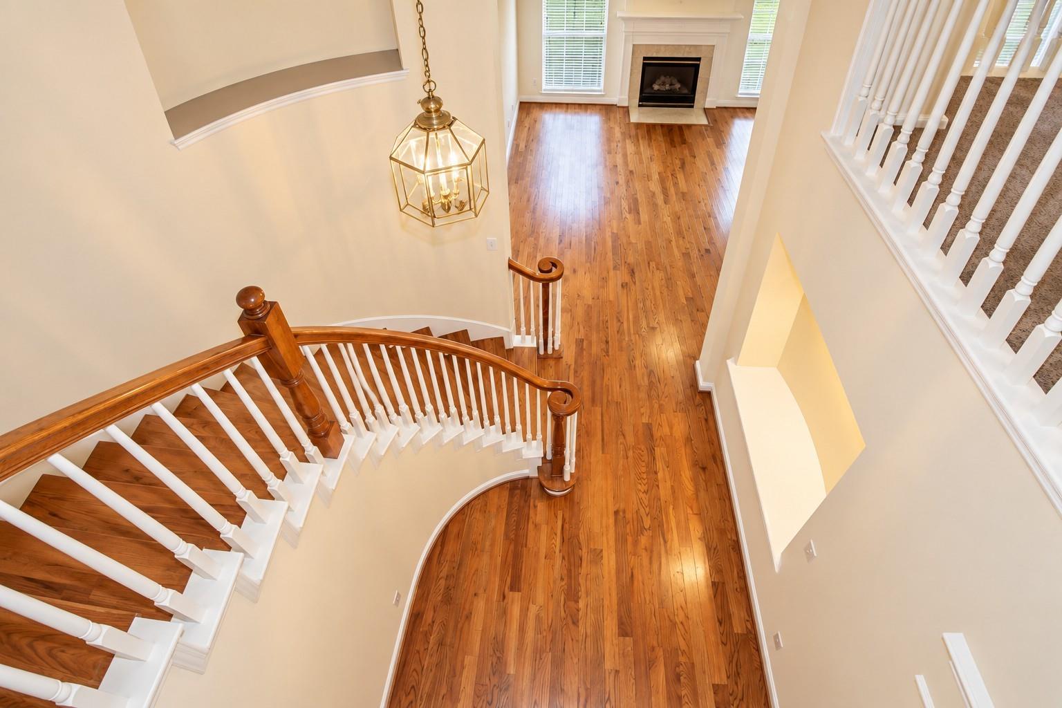 Two-story foyer with a curved hardwood staircase, lantern chandelier, and living room fireplace.