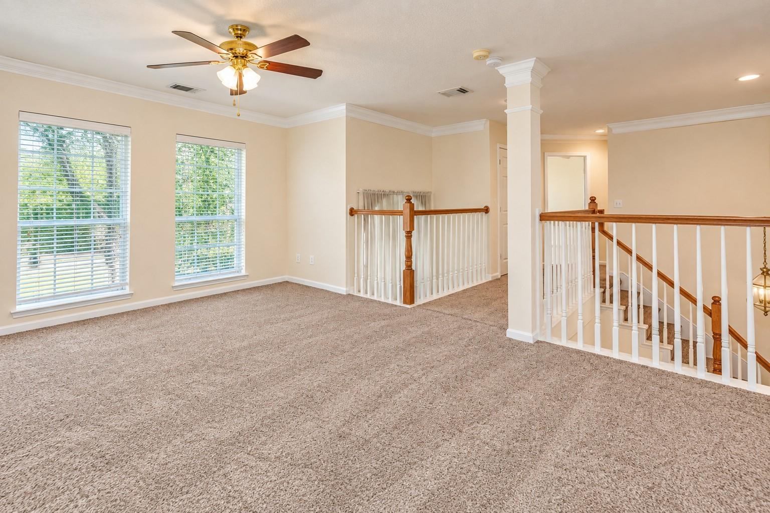 Carpeted upstairs loft with two windows, a ceiling fan, and railings overlooking the staircase.