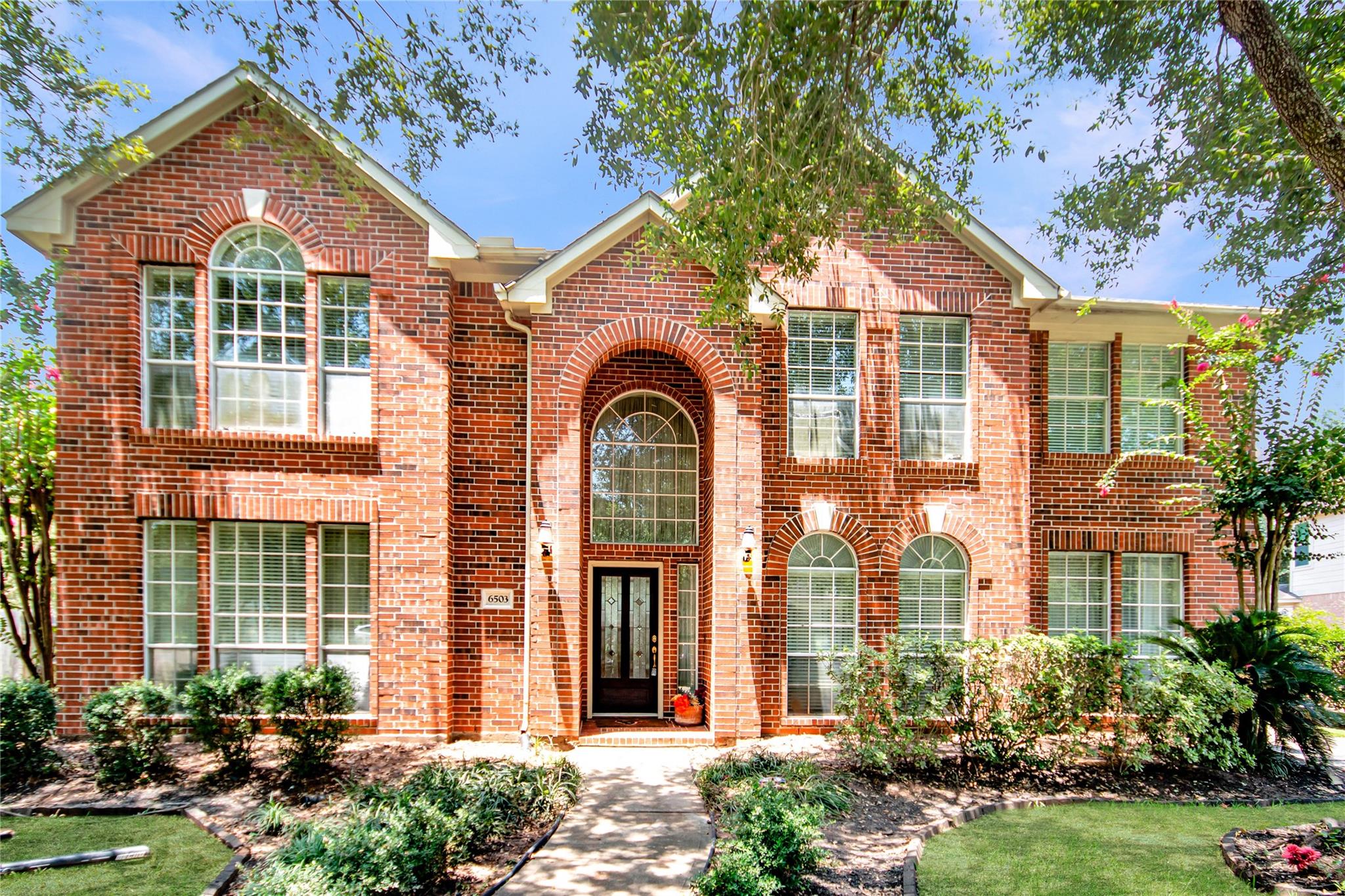 Two-story red brick home with an arched entry, arched windows, and landscaped front yard.