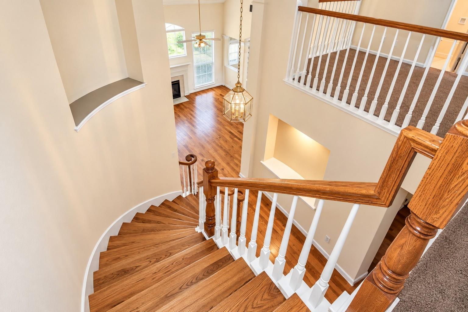 Curved hardwood staircase overlooking a bright foyer with a hanging lantern and fireplace.