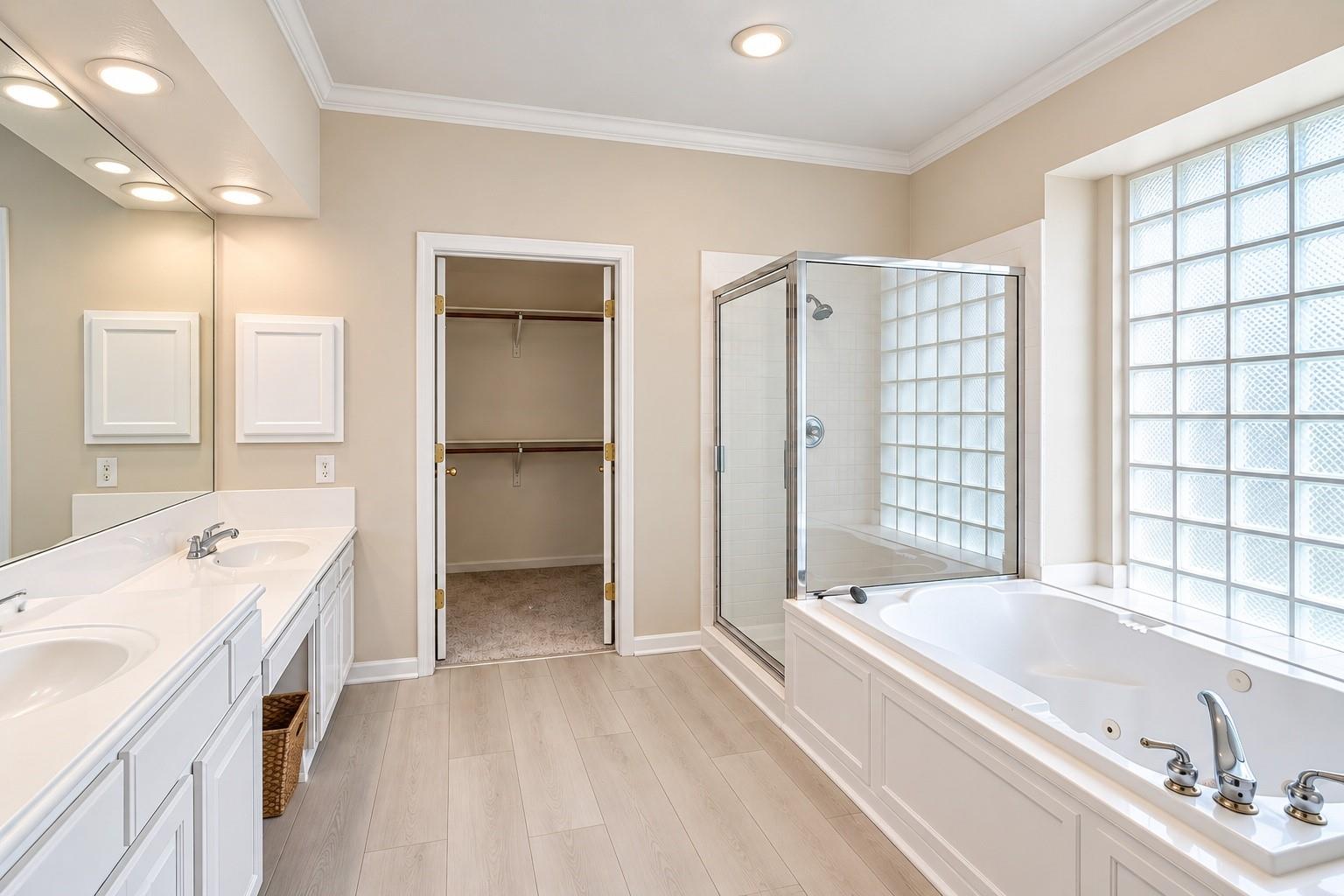 Primary bathroom with a double vanity, glass shower, jetted tub, and glass-block window.
