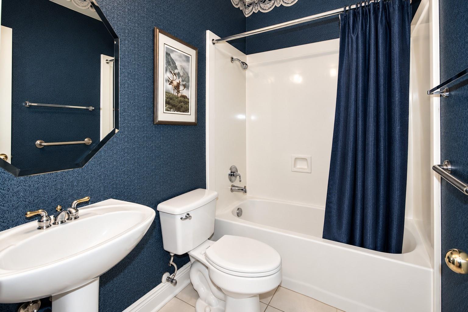 Bathroom with blue patterned wallpaper, a white tub and shower curtain, and a framed wildlife print.