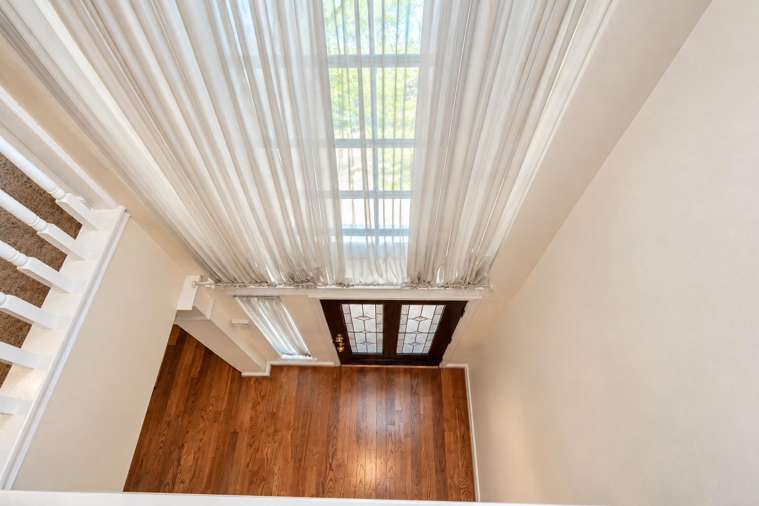 Entry foyer with a tall curtained window, hardwood floors, and a carpeted staircase.