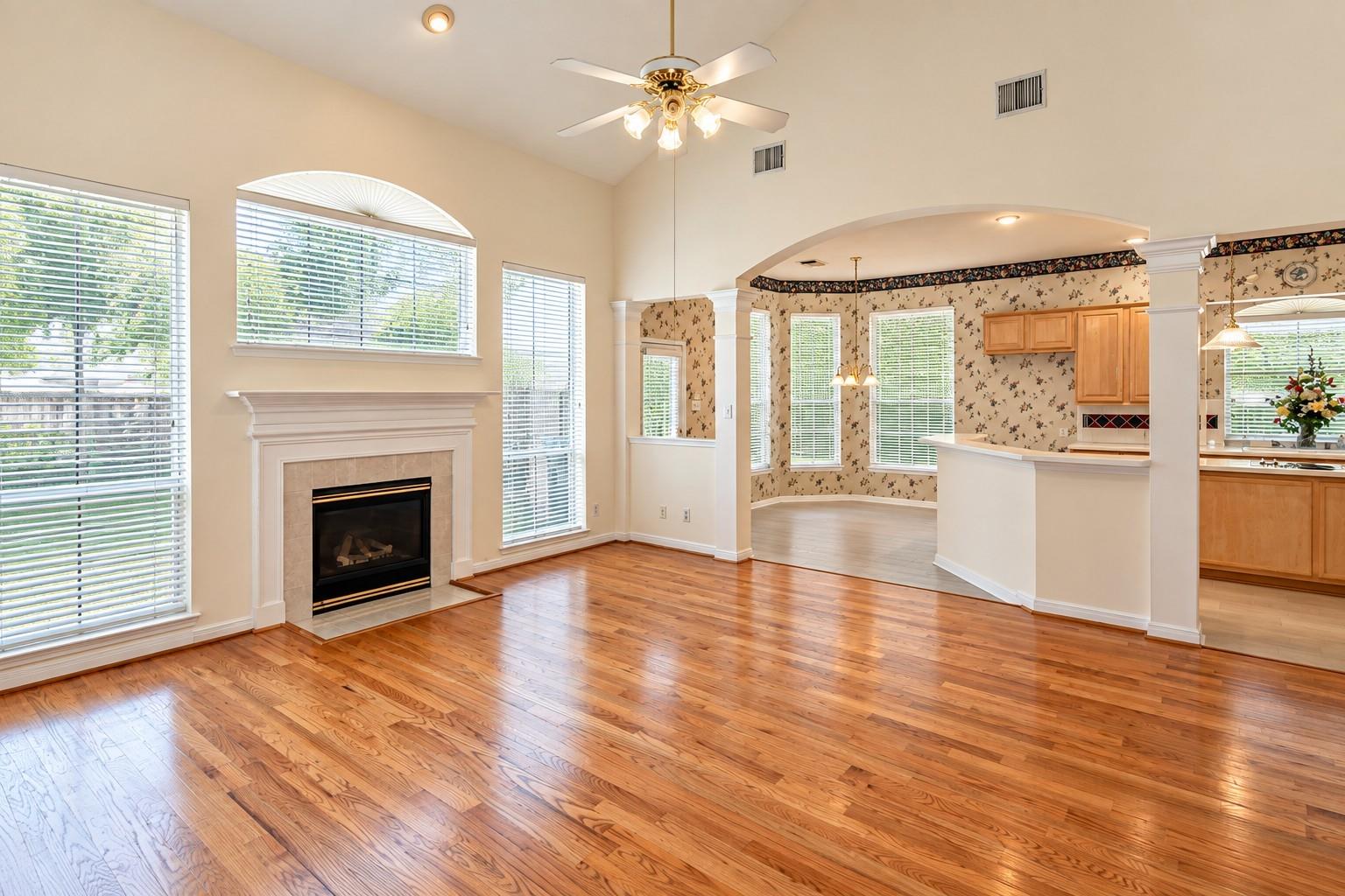Living room with polished hardwood floors, a white-trimmed fireplace, and an arched opening to the dining area.