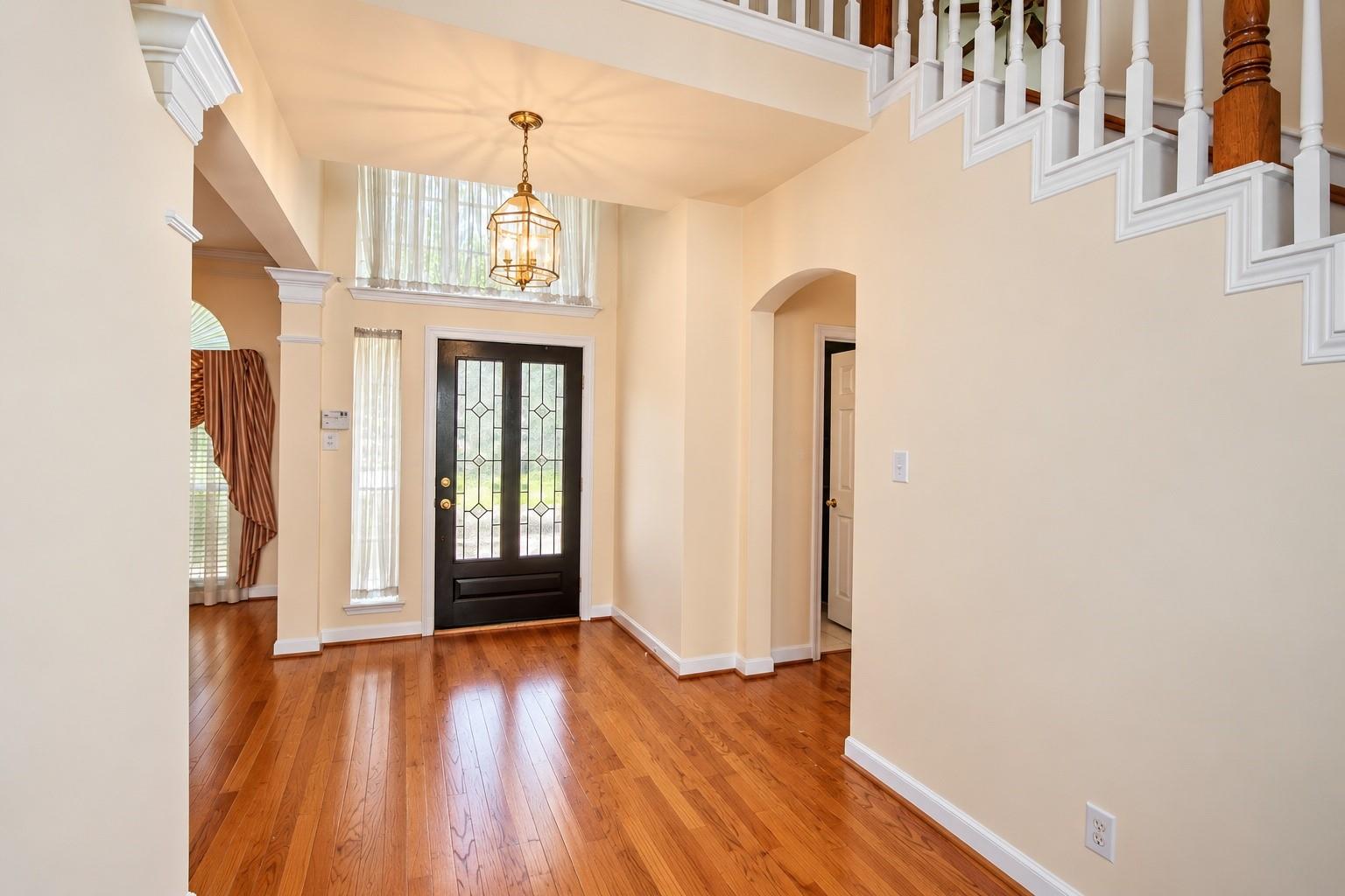 Two-story entry foyer with hardwood floors, a glass-paneled front door, and a white-railed staircase.