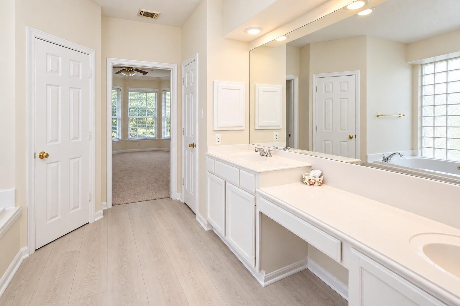 Bright bathroom with a long white double vanity and soaking tub beside a glass-block window.