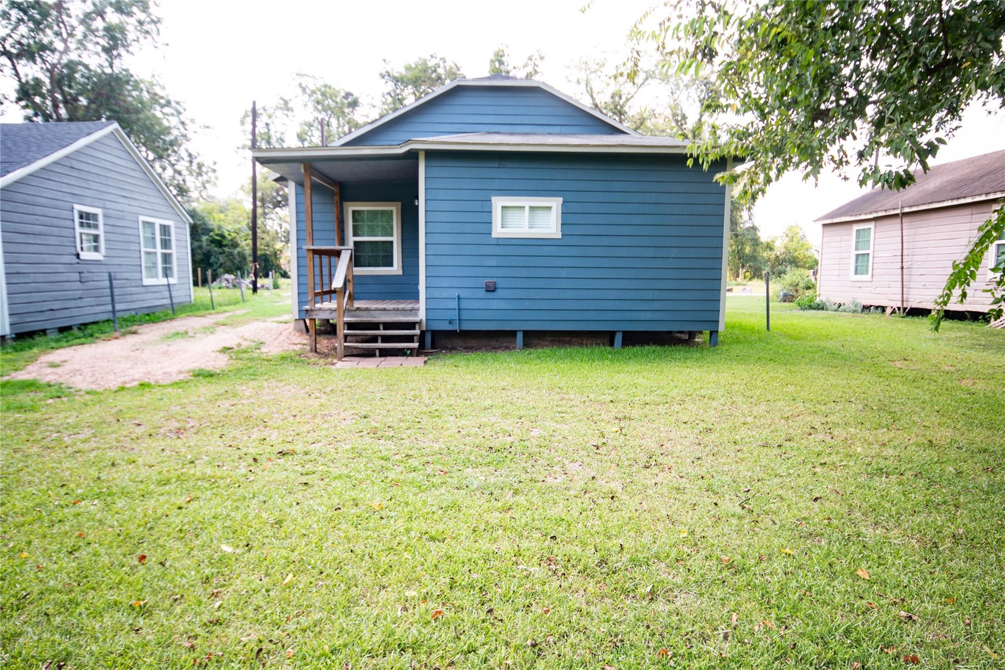 Blue house with a small raised porch and steps, seen beyond a broad lawn.
