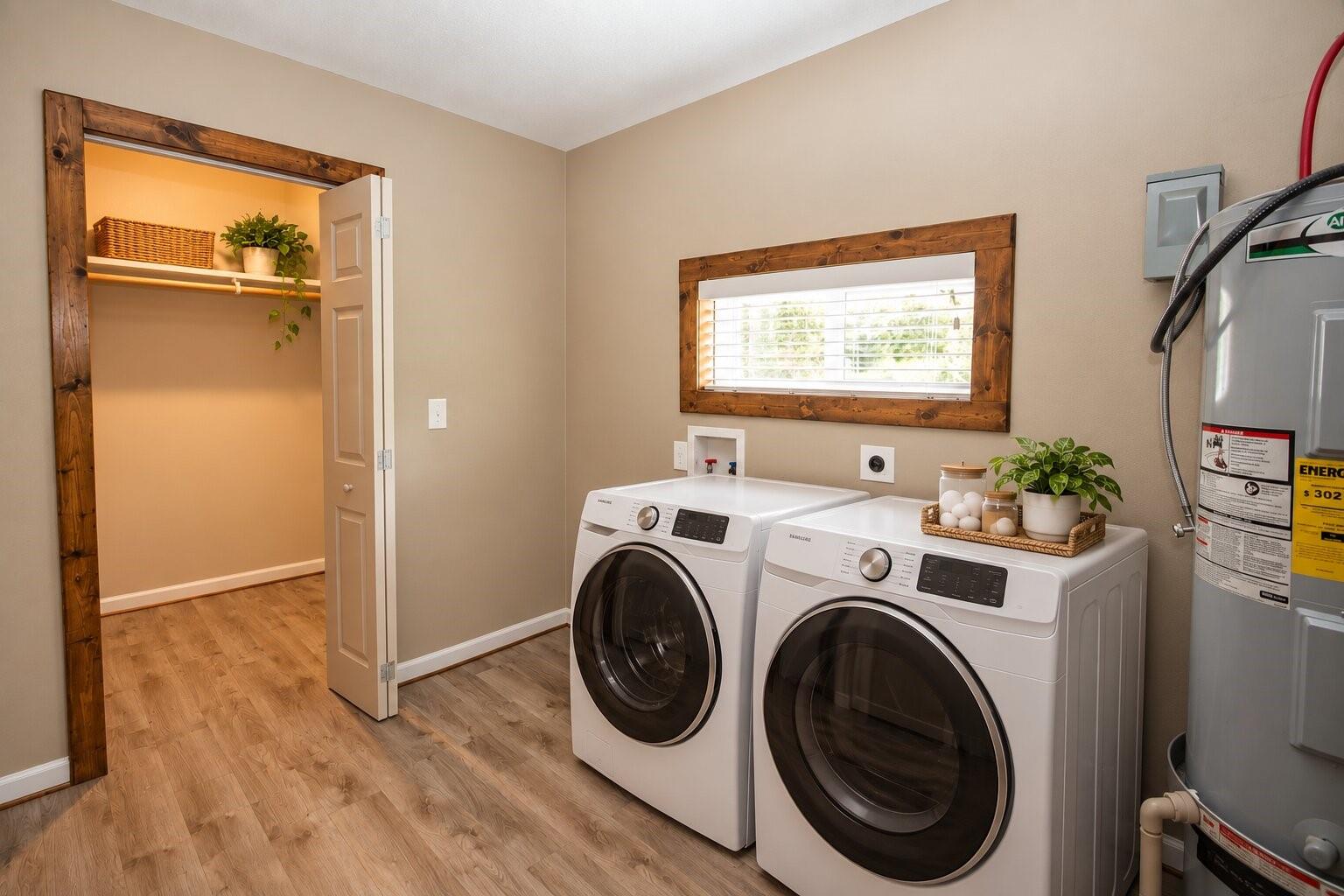 Laundry room with front-loading washer and dryer, wood-trimmed window, and adjacent water heater.
