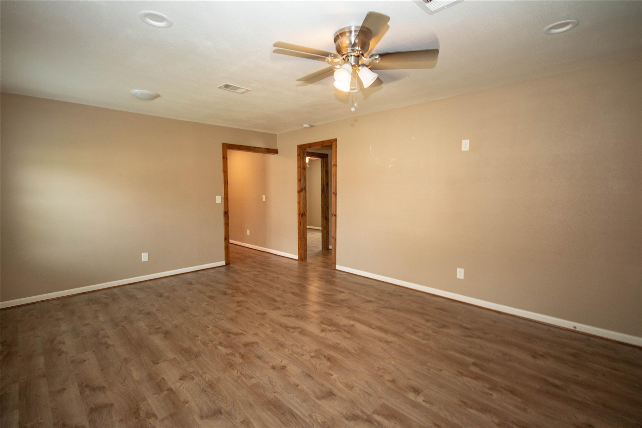 Empty room with wood-look flooring, natural wood door trim, and a lit ceiling fan.