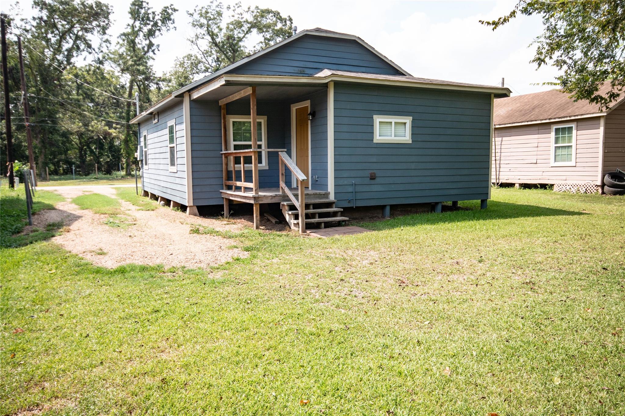 Blue-sided home with a covered wooden porch, steps, and broad grassy lawn.