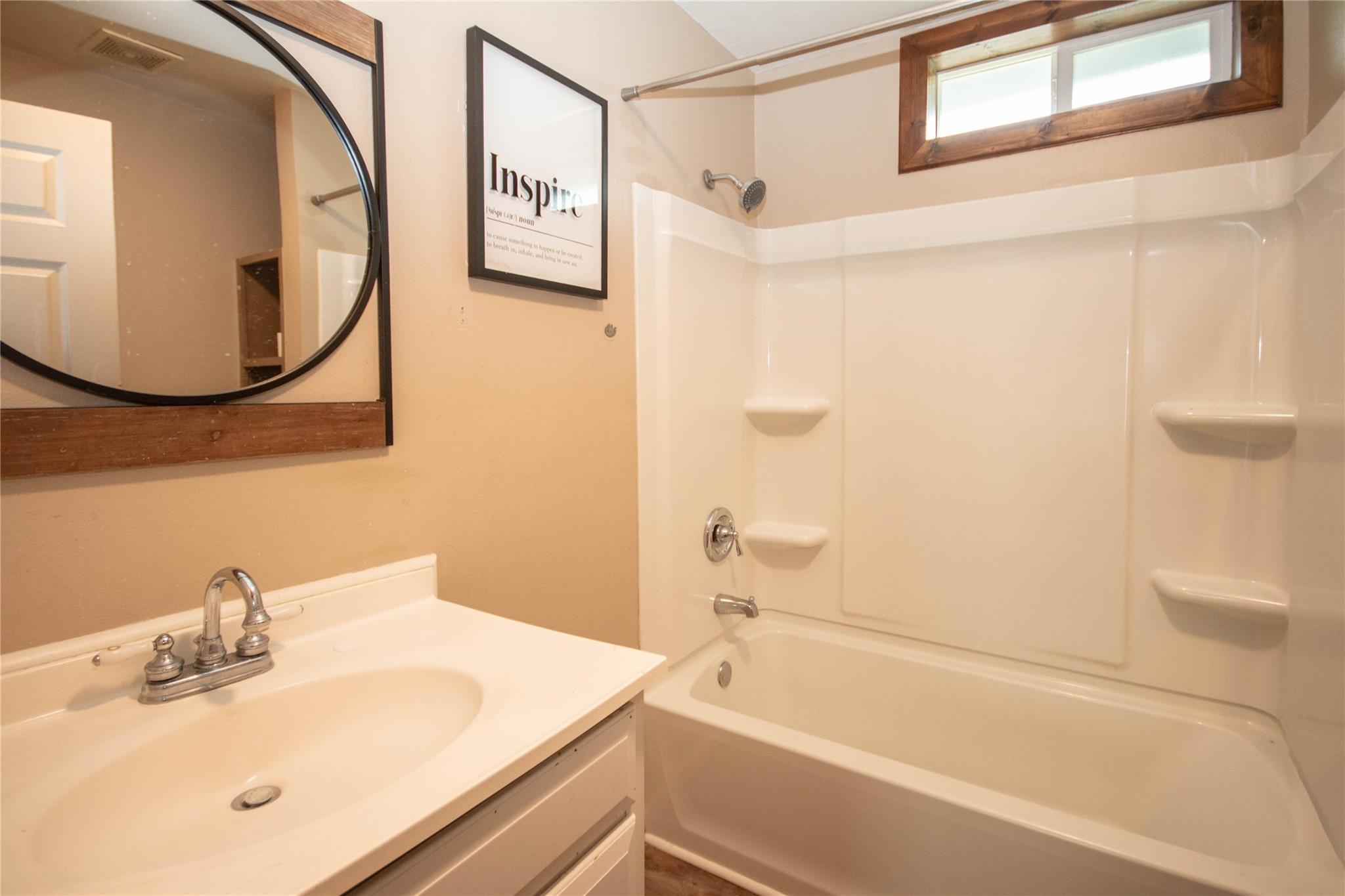 Bathroom with a white vanity, bathtub and shower, and a high horizontal window.