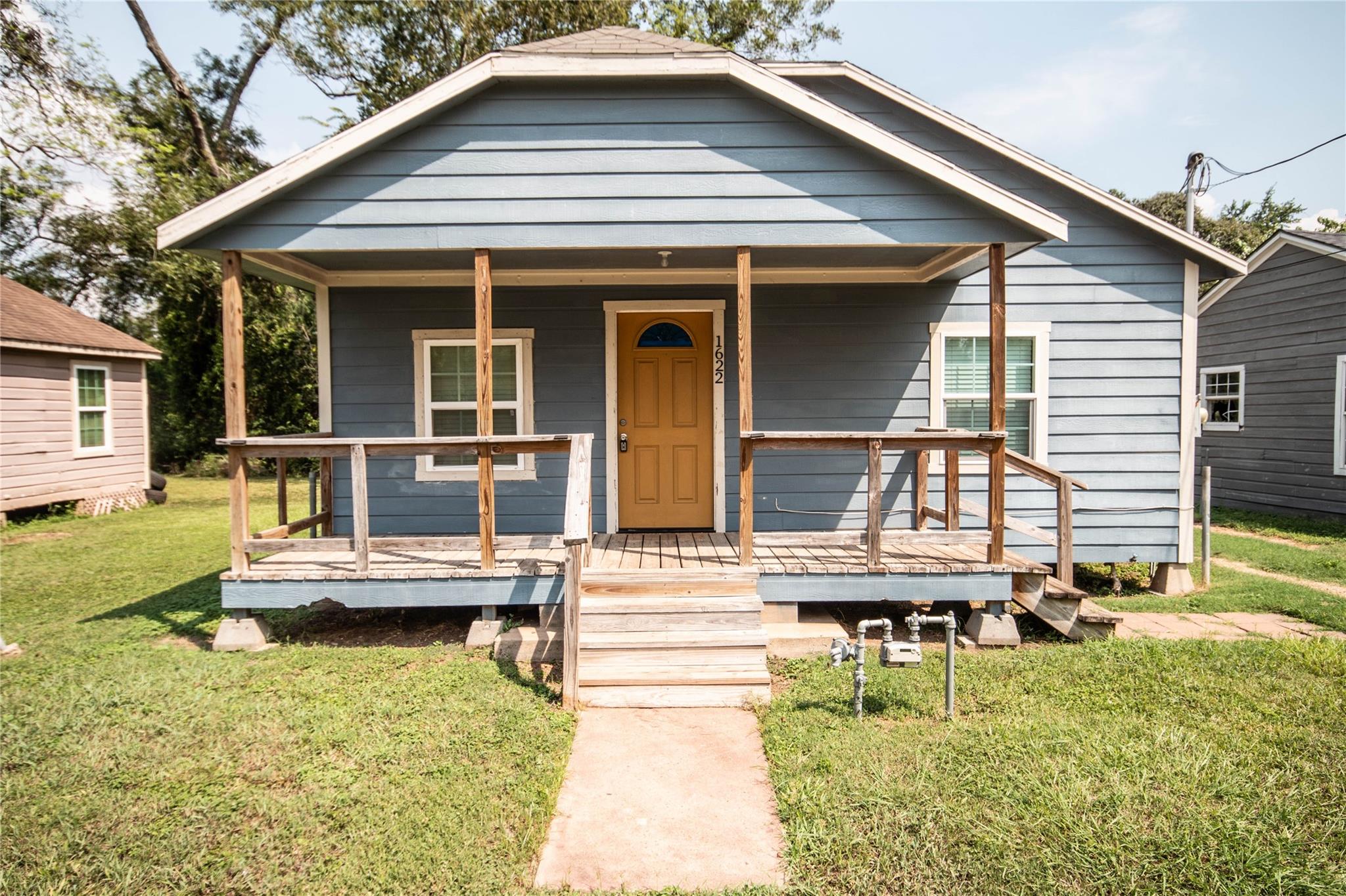 Blue-gray house with a mustard front door and broad covered wooden porch.