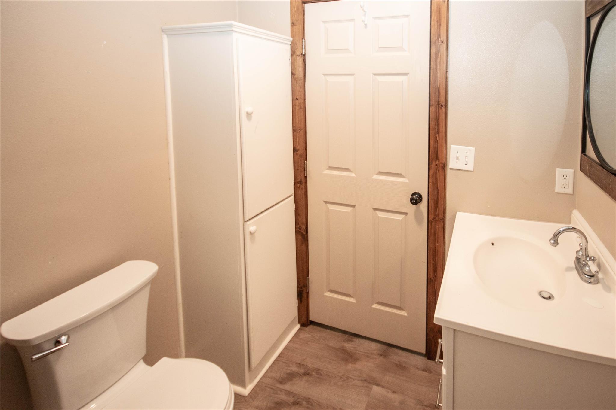 Bathroom with a toilet, white sink vanity, and tall storage cabinet beside the door.