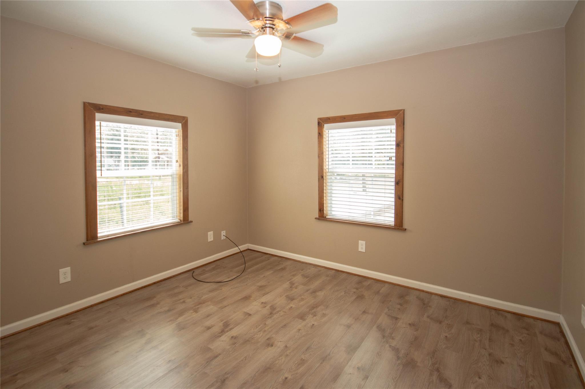 Empty room with wood-look flooring, two trimmed windows, and a ceiling fan with light.