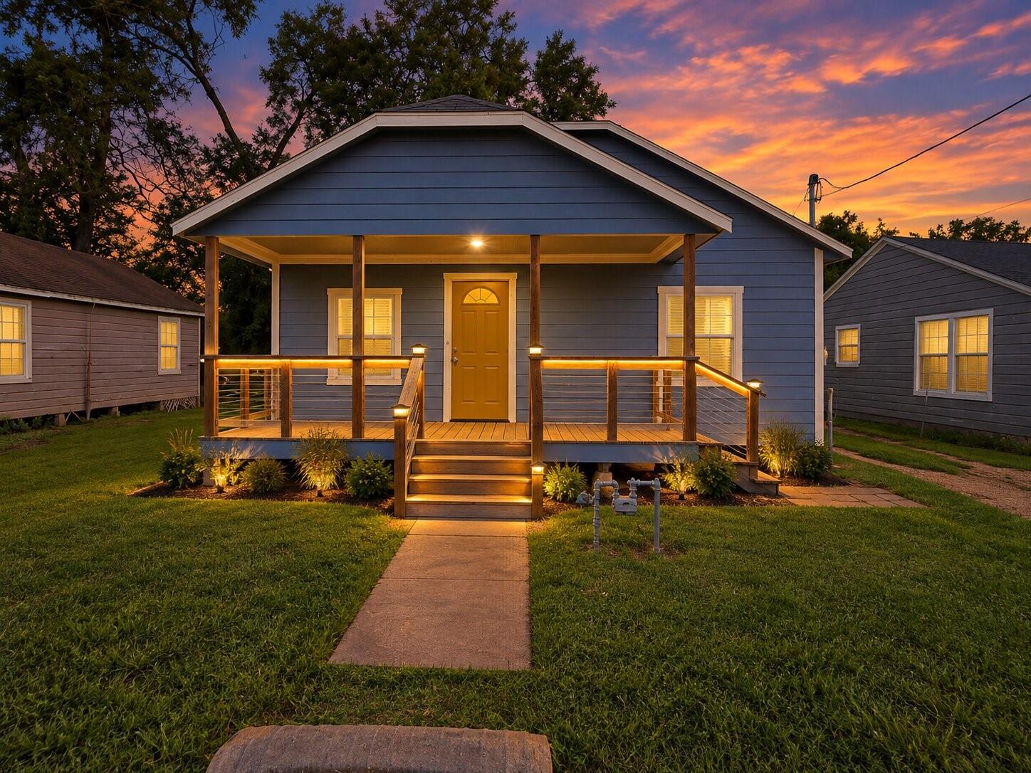 Blue single-story house with a warmly lit covered porch and front walkway at dusk.