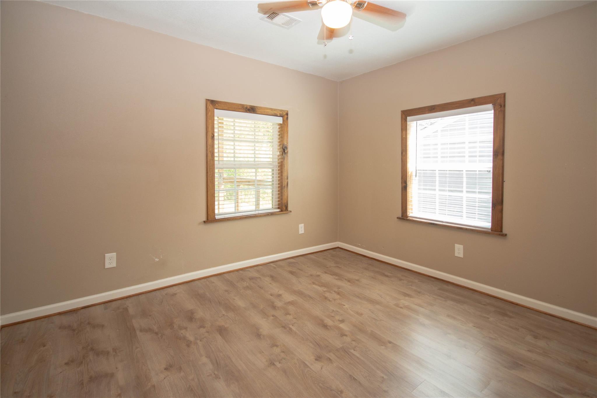 Empty room with wood-look flooring, two wood-trimmed windows, and a ceiling fan.