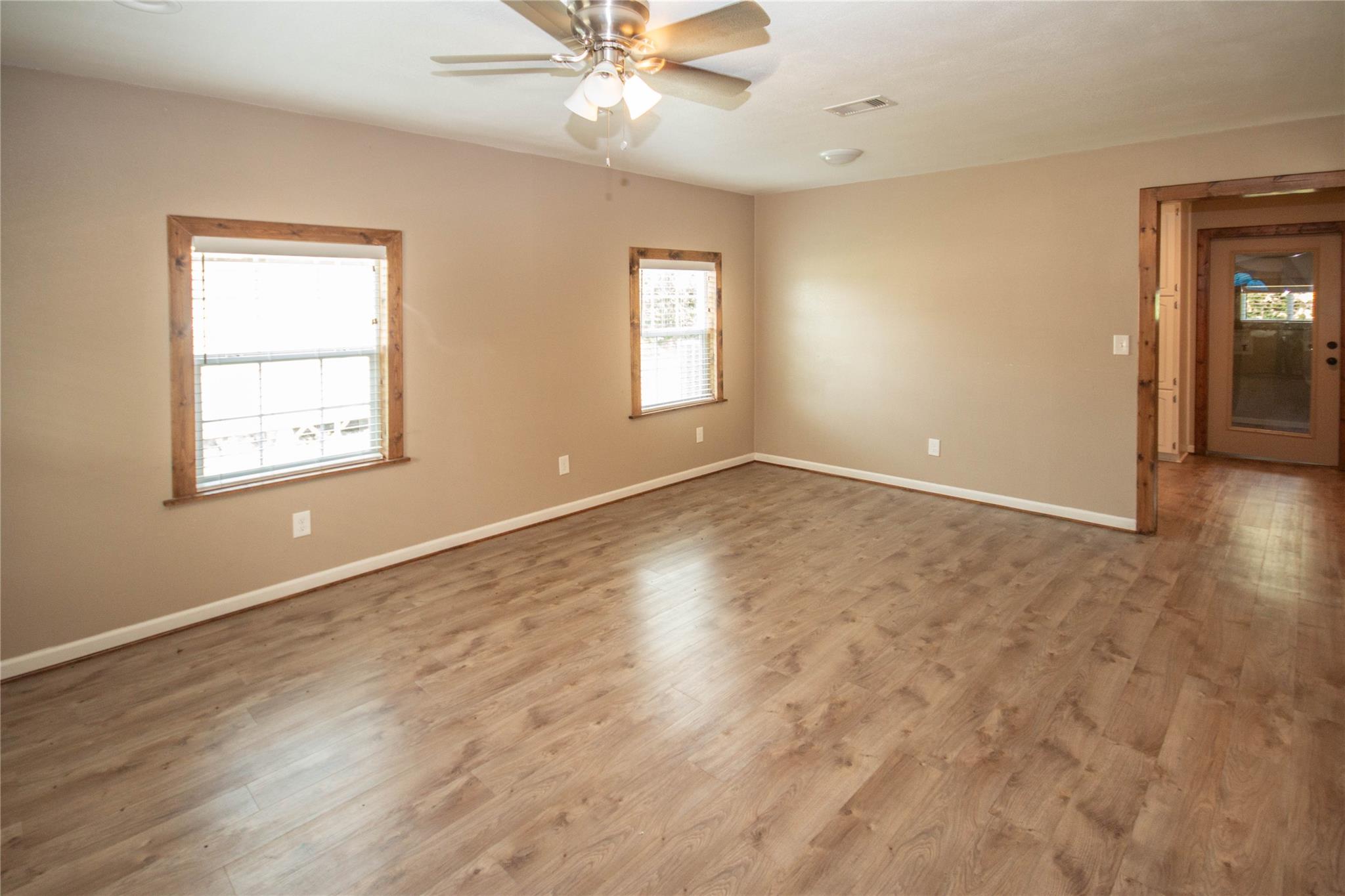 Empty living room with wood-look floors, two wood-trimmed windows, and a ceiling fan.