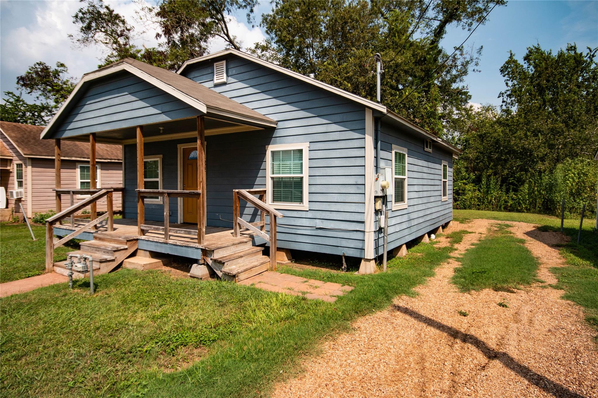 Blue house with a covered wooden porch, grassy yard, and gravel driveway.