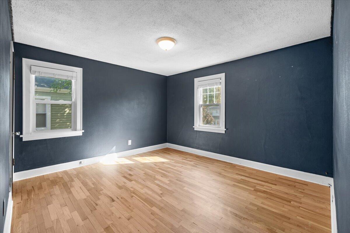 Empty room with navy walls, two windows, and a light hardwood floor.