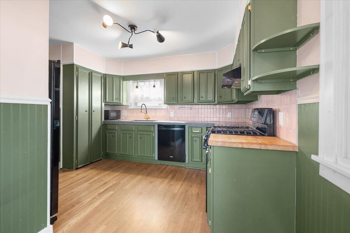 Kitchen with sage green cabinets, pink tile backsplash, and wood flooring.