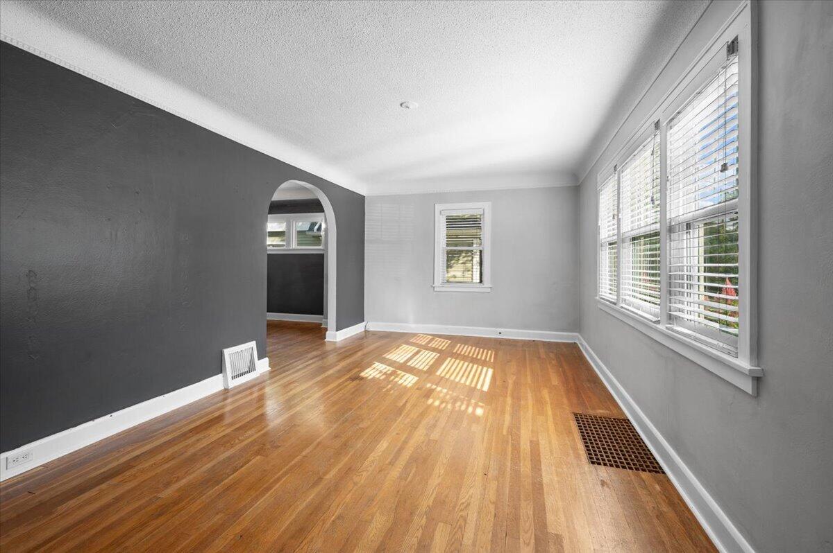 Empty room with hardwood floors, a charcoal accent wall, arched doorway, and large windows.