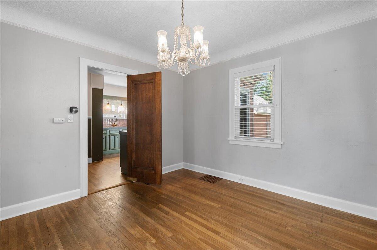 Unfurnished dining room with hardwood floors, a crystal chandelier, and an open doorway to the kitchen.