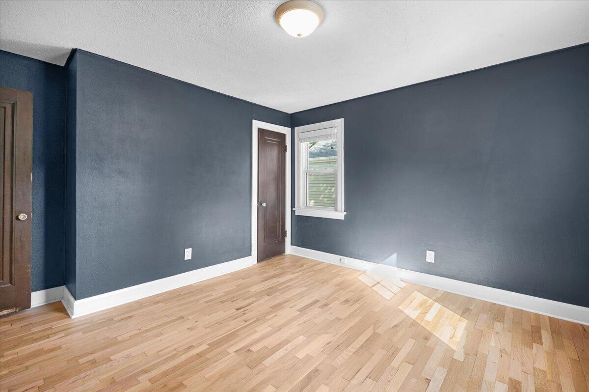 Unfurnished room with dark blue walls, light hardwood floors, and a white-trimmed window.