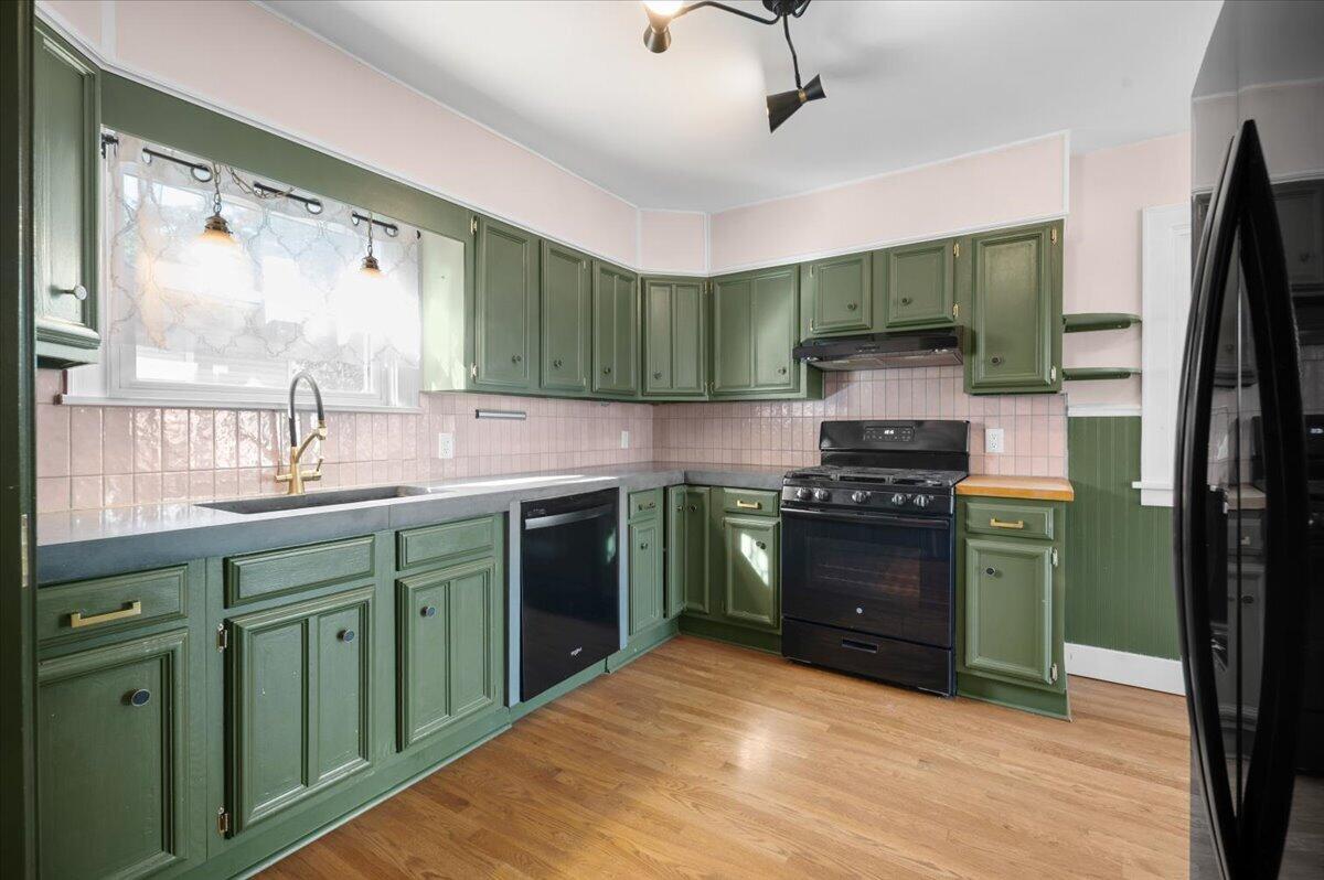 Kitchen with sage-green cabinets, pink tile backsplash, and a window over the sink.