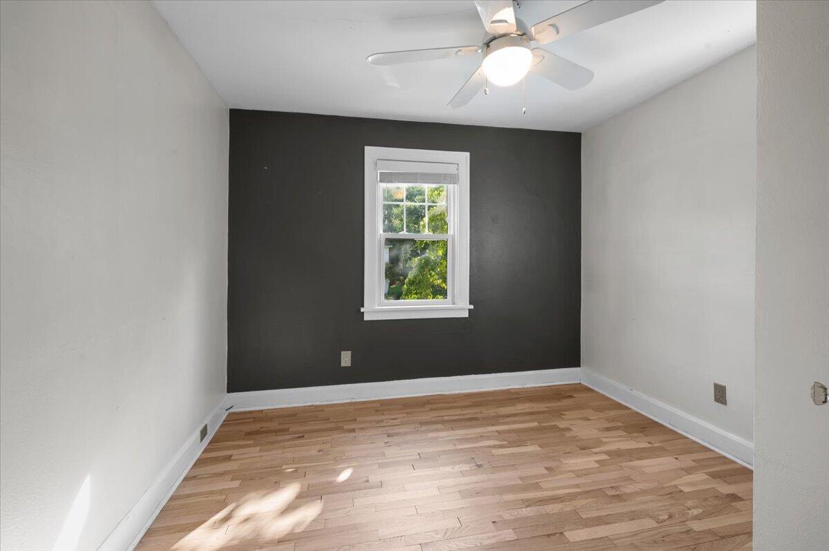 Empty room with hardwood floors, a charcoal accent wall, and a window.