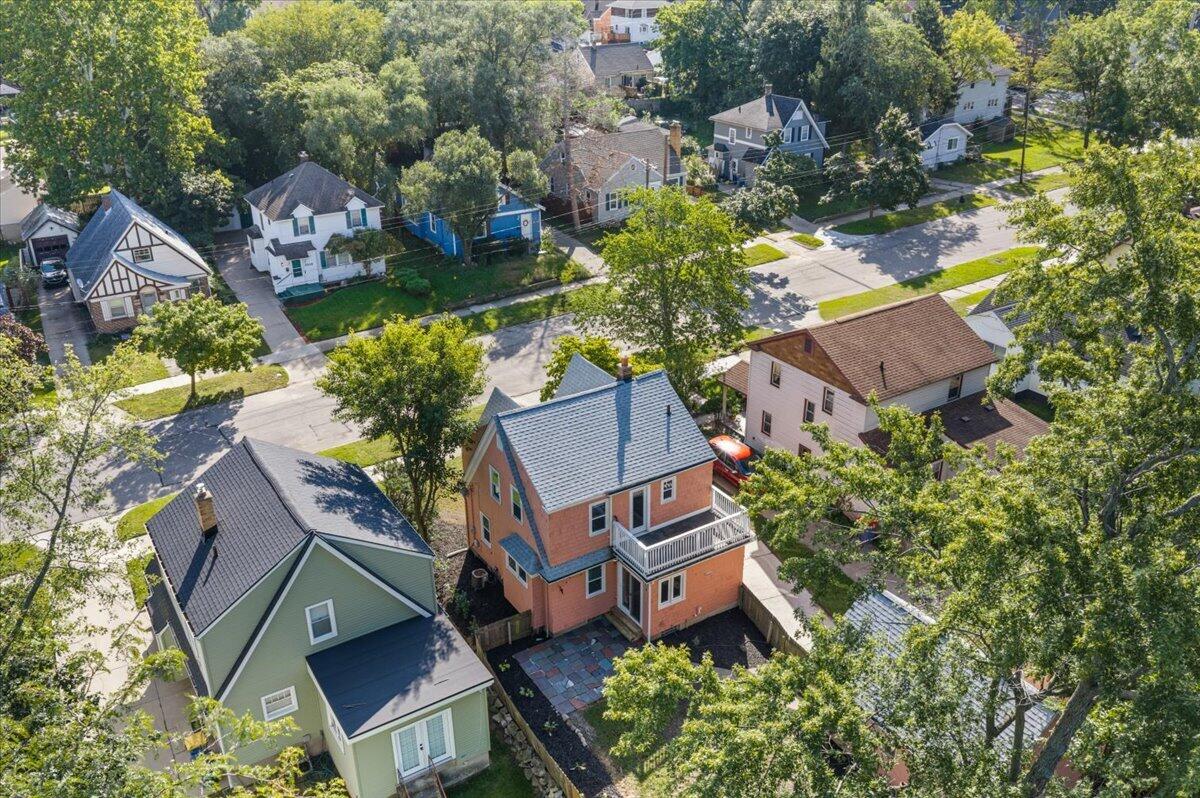 Aerial view of an orange two-story house with a white balcony and paved patio among leafy neighborhood homes.
