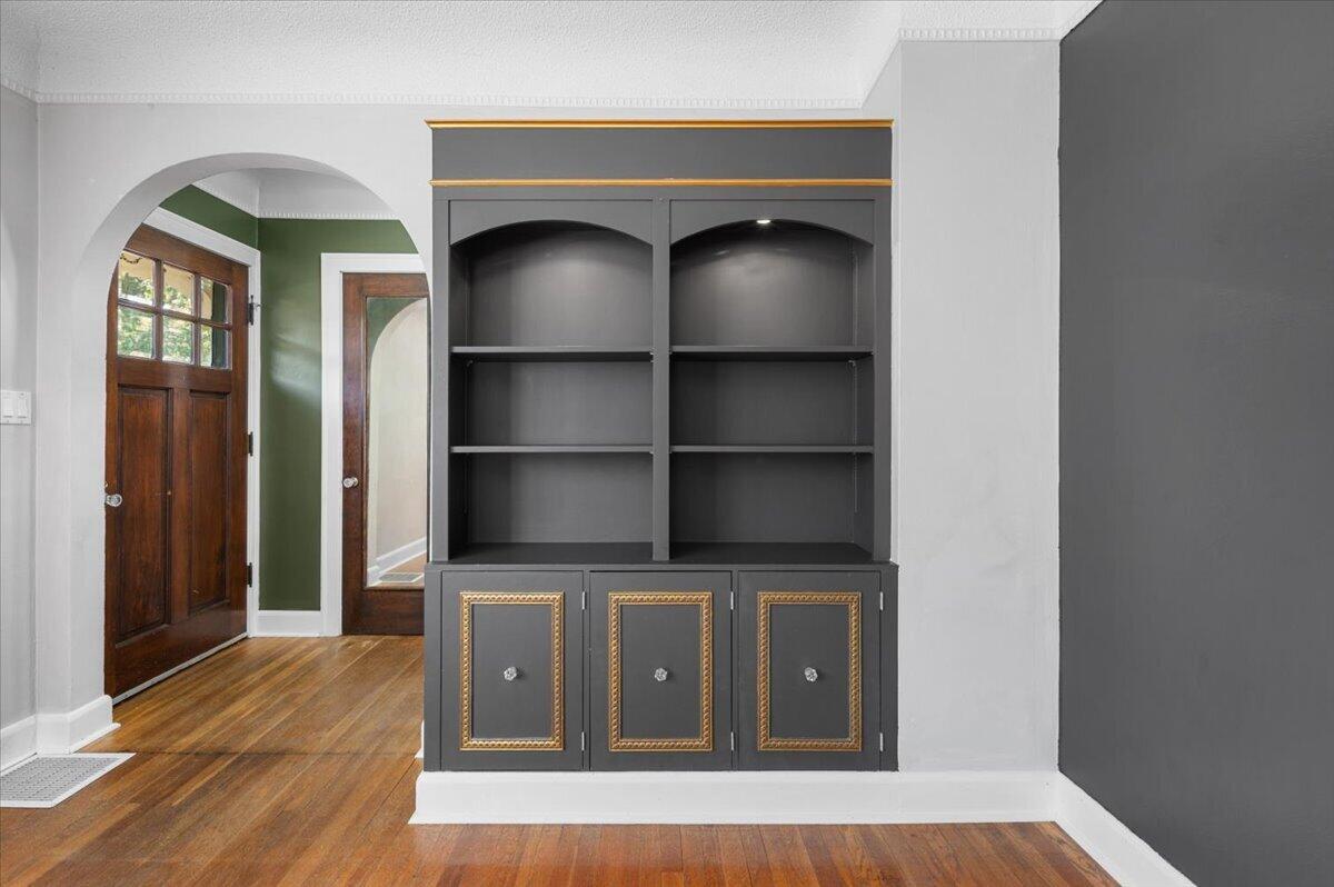 Entryway with built-in gray shelving and gold-trimmed cabinets beside a wood front door.