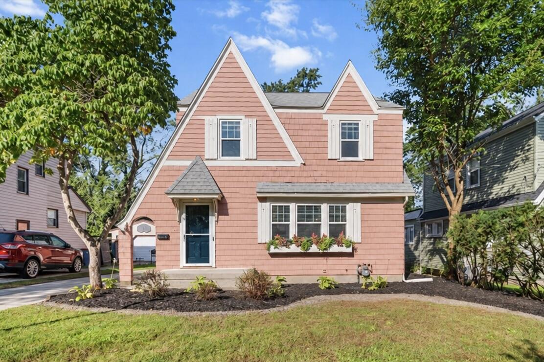 Pink two-story house with twin front gables, a teal door, and a flower box.