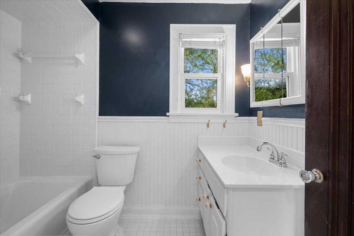 Bathroom with a tiled tub and shower, white vanity, and navy walls above white beadboard.