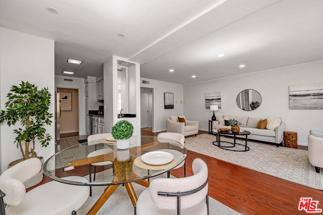 Living and dining area with a glass table, white upholstered chairs, neutral seating, and hardwood floors.