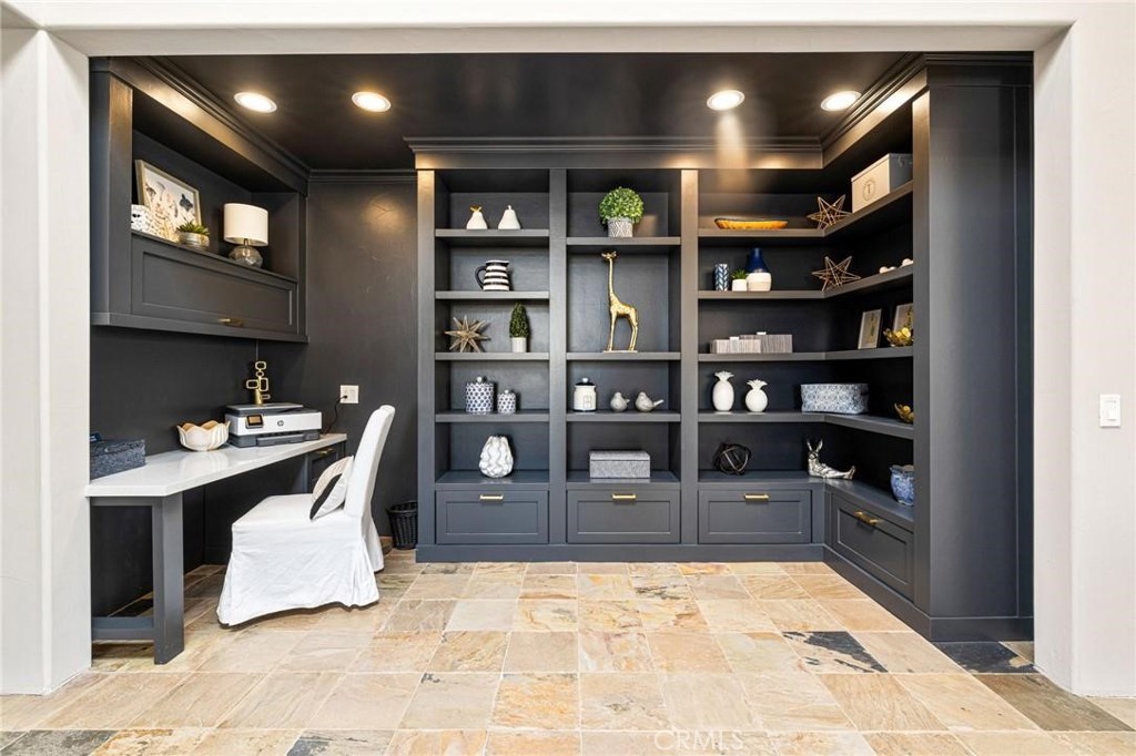 Home office with dark built-in shelves, a white desk and chair, and stone-tile flooring.