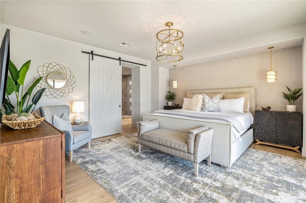 Furnished bedroom with an upholstered bed, gold chandelier, and white sliding barn door.