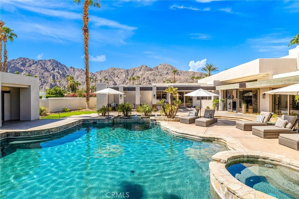 Desert home with a turquoise pool and raised spa, furnished patio, and mountain backdrop.