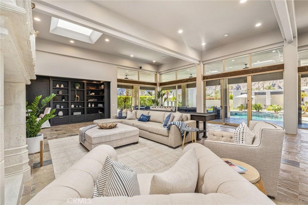 Living room with a large sectional, dark built-in shelves, and windows overlooking a pool.