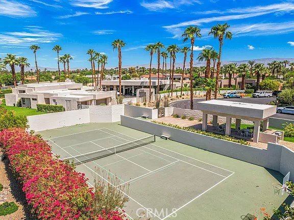 Aerial view of a tennis court and modern homes among palm trees.